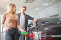 Young smiling family couple buying first electric car in the showroom. Close-up of attractive woman charging ecological