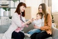 Young smiling female doctor examining little baby girl on mother`s arms at home Royalty Free Stock Photo