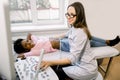 Young smiling female doctor moving ultrasound transducer on African woman belly and kidneys while looking at screen in Royalty Free Stock Photo