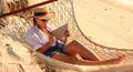 Young smiling female, happy woman in straw hat and sunglasses using digital tablet while relaxing in the hammock on tropical sandy Royalty Free Stock Photo