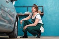 Young smiling female mechanic in blue coveralls squatting near tire and holding ratchet wrench. The concept of Royalty Free Stock Photo