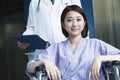 Young smiling female patient sitting in a wheelchair, doctor standing behind her, looking at camera Royalty Free Stock Photo