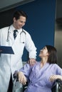 Young smiling female patient sitting in a wheelchair, looking up at doctor standing beside her Royalty Free Stock Photo