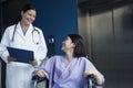 Young smiling female patient sitting in a wheelchair, looking up at the doctor standing beside her Royalty Free Stock Photo