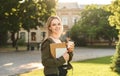 Young smiling female student holding take away coffee in the park near the college. Pretty, cute casual student near the high Royalty Free Stock Photo