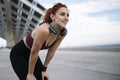 Young smiling fit woman in sportswear resting after run wearing headphones. Athletic female listening music taking a