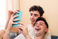 Young smiling gay couple using the smart phone to watch entertaining content. LGBT people routine