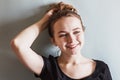 A young smiling girl adjusts her hair with her hand against the blue wall