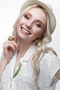 Young smiling girl with curls in a hat. A beautiful model in a white shirt and a brooch-flower Royalty Free Stock Photo