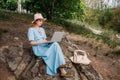 A young smiling girl freelancer works with a laptop in nature.