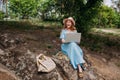 A young smiling girl freelancer works with a laptop in nature