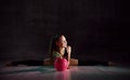 Young smiling girl gymnast in black sport body and uppers sitting in twine on floor and holding pink gymnastic ball in hands