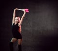 Young smiling girl gymnast in black sport body and uppers standing and holding two pink gymnastic maces in raised hands