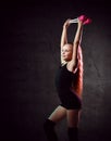 Young smiling girl gymnast in black sport body and uppers standing and holding two pink gymnastic maces in raised hands