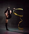 Young smiling girl gymnast in black sport body and uppers standing and making exercise with yellow gymnastic tape