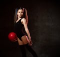 Young smiling girl gymnast with long hair in black sport body and uppers standing and holding pink gymnastic ball in hand