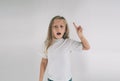 Young smiling girl having a good idea. Portrait of an excited child in white T-shirt pointing finger up at copyspace