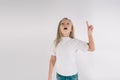 Young smiling girl having a good idea. Portrait of an excited child in white T-shirt pointing finger up at copyspace