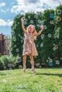 young smiling girl with long wavy fair hair in sparkling dress jumping, catching soap bubbles .