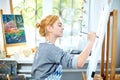 Young smiling girl paints on canvas with oil colors in own workshop. Window on the background. Art concept. Royalty Free Stock Photo