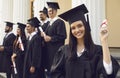 Young smiling girl university graduate standing holding diploma in raised hand over group of mates Royalty Free Stock Photo