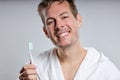 young smiling guy brushing tooth, wearing bathrobe, isolated on gray studio background Royalty Free Stock Photo