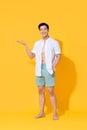 Smiling handsome Asian man in beach attire doing open palm gesture showing blank space  in summer yellow  studio Royalty Free Stock Photo