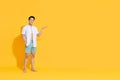 Smiling handsome Asian man in beach attire doing open palm gesture showing blank space  in summer yellow  studio Royalty Free Stock Photo