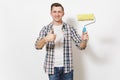 Young smiling handsome man in casual clothes holding paint roller for wall painting and showing thumb up isolated on Royalty Free Stock Photo