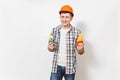 Young smiling handsome man in casual clothes and protective orange hardhat holding toy hammer and saw isolated on white Royalty Free Stock Photo