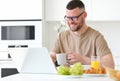 Young smiling handsome man working remotely on laptop in modern kitchen at home Royalty Free Stock Photo