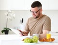 Young smiling handsome man working remotely on tablet in modern kitchen at home Royalty Free Stock Photo