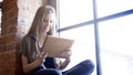 Young smiling happy attractive woman holding a digital tablet sitting on the window sill Royalty Free Stock Photo