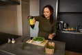 Young smiling happy woman adding olive oil into bowl with fresh vegetable salad on table in the home kitchen Royalty Free Stock Photo