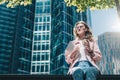 Young smiling hipster businesswoman in glasses sits outdoors and holding digital tablet and cup of coffee. Royalty Free Stock Photo