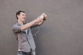 Young smiling hipster man taking selfie with his smartphone. Gray background, copy space