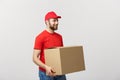 Young smiling logistic delivery man in red uniform holding the box on white background