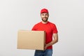 Young smiling logistic delivery man in red uniform holding the box on white background