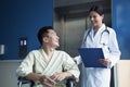 Young smiling male patient sitting in a wheelchair, looking up at the doctor standing beside him Royalty Free Stock Photo