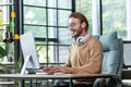 Young smiling male student in headphones sits on campus at a desk and studies online at a computer. Writes coursework Royalty Free Stock Photo