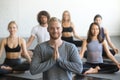 Young smiling male yoga instructor and group in lotus pose