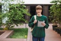 Young smiling man with backpack standing and happily looking in camera with tablet in hand in courtyard of university Royalty Free Stock Photo