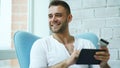 Young smiling man doing online shopping using digital tablet computer sitting at balcony at home Royalty Free Stock Photo