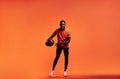 Young smiling man dribbling a basket ball over an orange background in studio Royalty Free Stock Photo