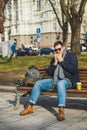 young smiling man eating burger and drink coffee sitting on city bench