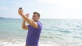 Young smiling man having a video call on smart phone at the sea beach. Happy guy making video online chats on beautiful Royalty Free Stock Photo