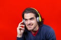 Young smiling man isolated on a redbackground listening to music with bright yellow headphones.