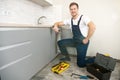 Young smiling man plumber in uniform fixing the sink with adjustable spanner in his hand working in the kitchen Royalty Free Stock Photo