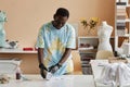 Young smiling man in protective gloves rolling white t-shirt on table