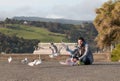 Young smiling man sits on the ground and feeds seagulls , Akaroa, New Zealand